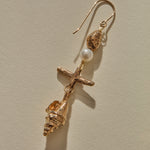 Close view of a Sereia Shell and Pearl Chandelier Earring in bronze, the pearl above the ridged spiral shell.