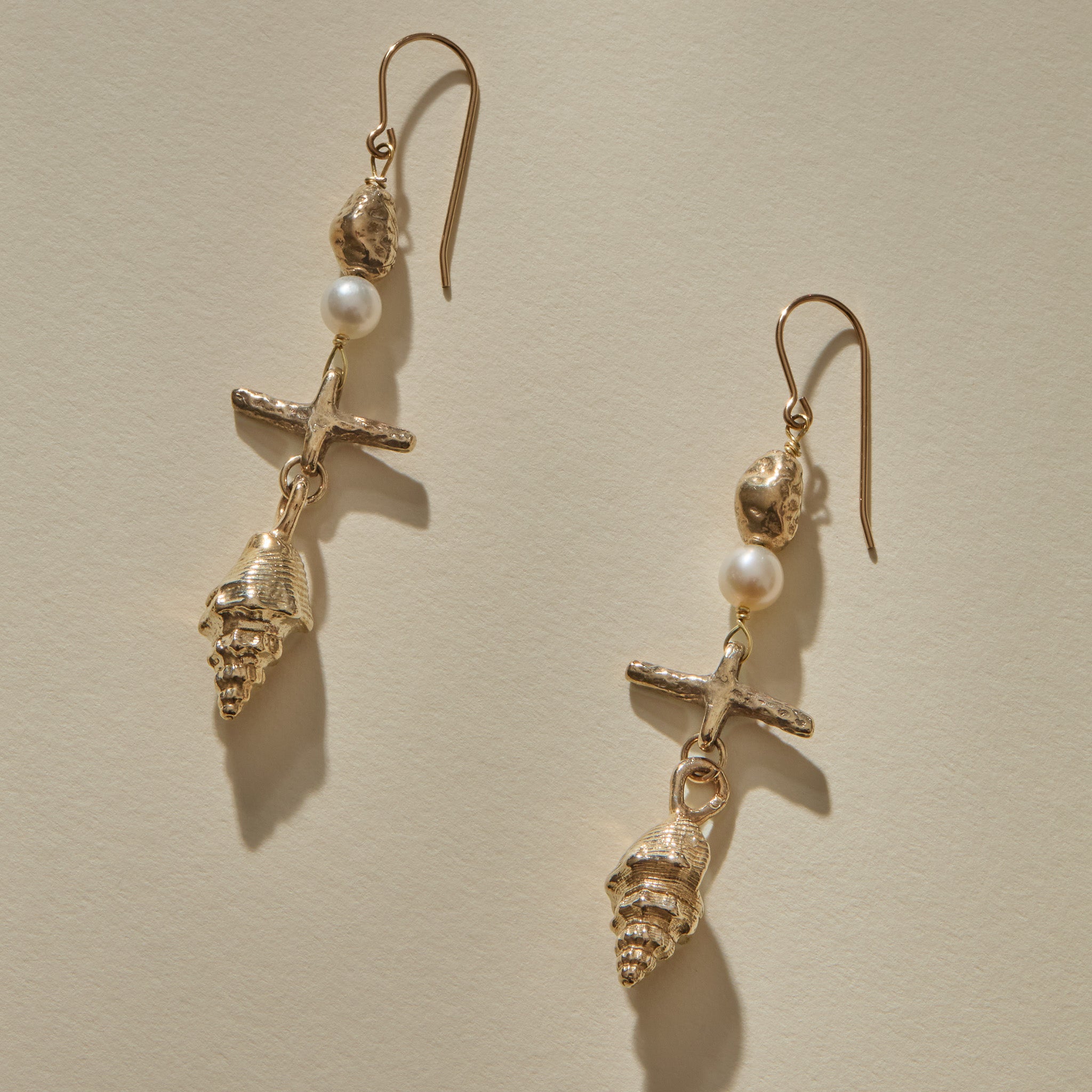 Sereia Shell and Pearl Chandelier Earrings in gold laid at an angle, the pearls catching the light.