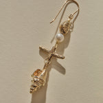 Close view of a Sereia Shell and Pearl Chandelier Earring in gold, the pearl above the ridged spiral shell.