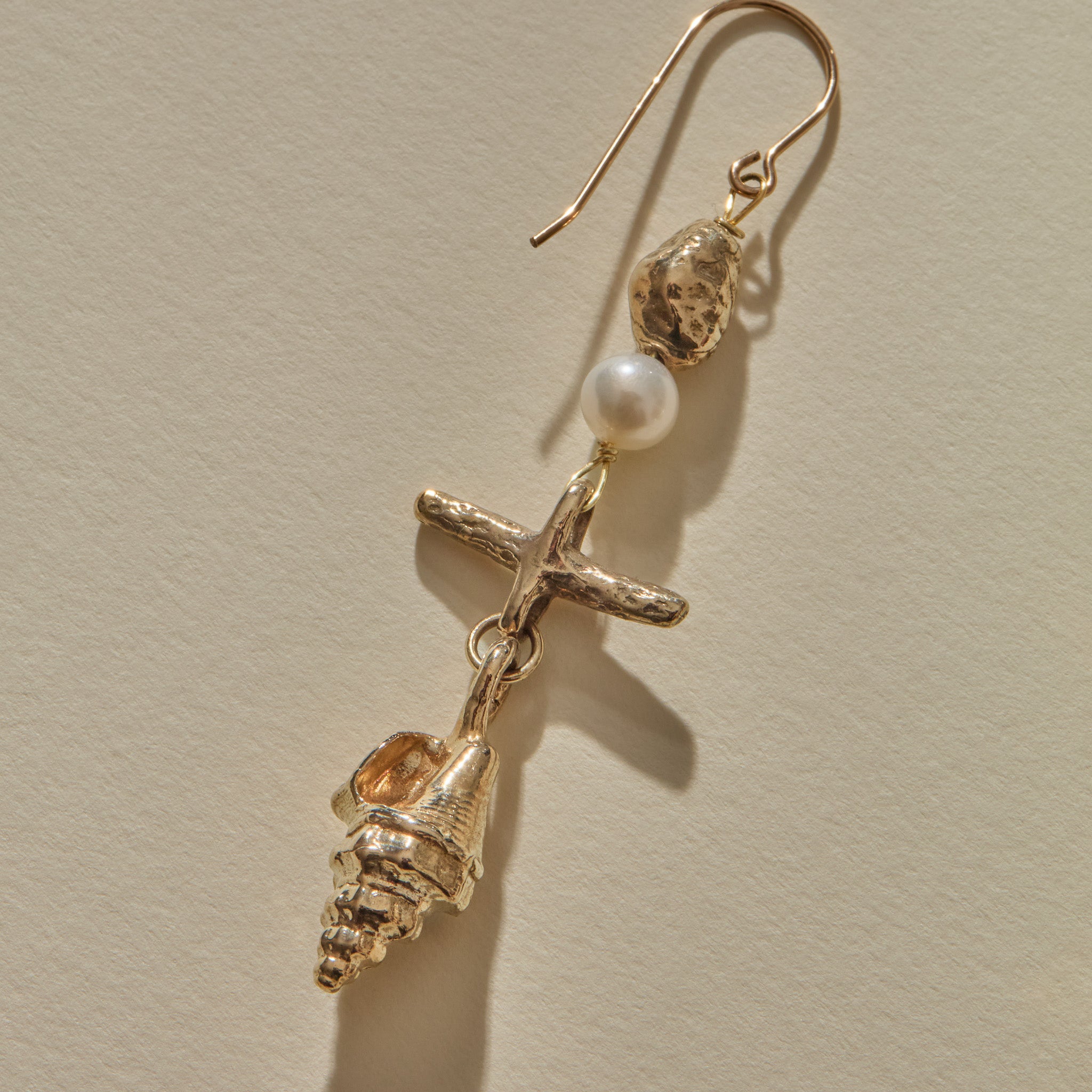 Close view of a Sereia Shell and Pearl Chandelier Earring in gold, the pearl above the ridged spiral shell.