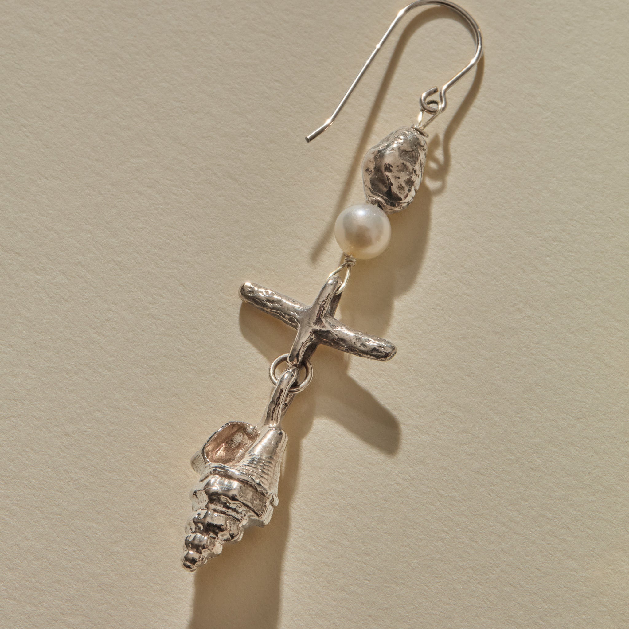 Close view of a Sereia Shell and Pearl Chandelier Earring in sterling silver, the pearl above the ridged spiral shell.