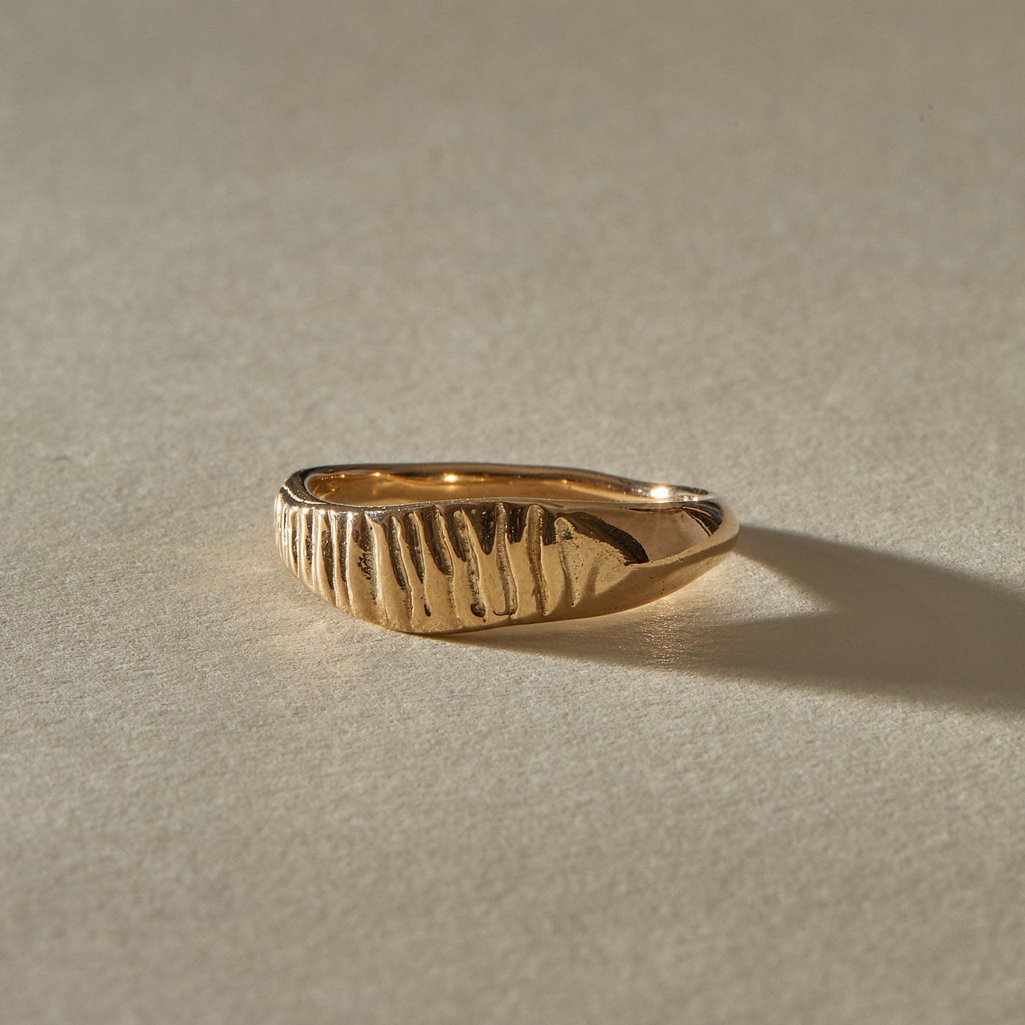 Smoke Ring in solid gold from the side, showing the carved smoke lines tapering into a slim band.