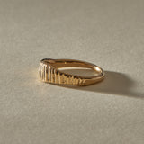 Smoke Ring in solid gold in low light, its carved vertical lines catching a soft glow.