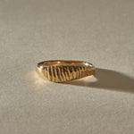 Smoke Ring in solid recycled gold, with flickering vertical lines carved across a sculpted signet face, in warm sunlight.