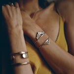 Model in a yellow top wearing the Sunkeeper and Pyramids cuffs in bronze stacked on one wrist.