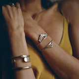 Model in a yellow top wearing the Sunkeeper and Pyramids cuffs in bronze stacked on one wrist.