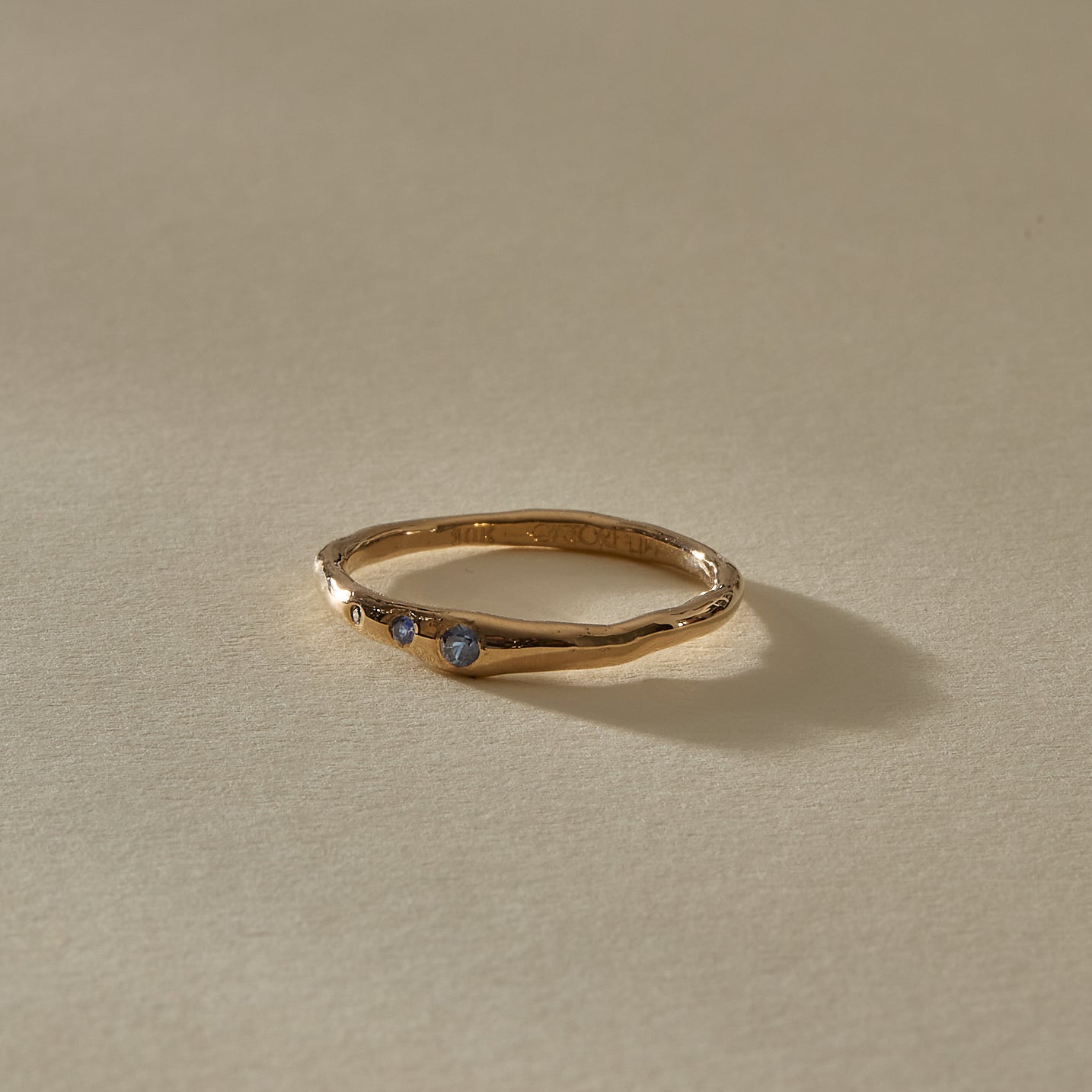 Vida Sapphire Ring from the front, showing three tiny blue sapphires set along the gently curved gold band.