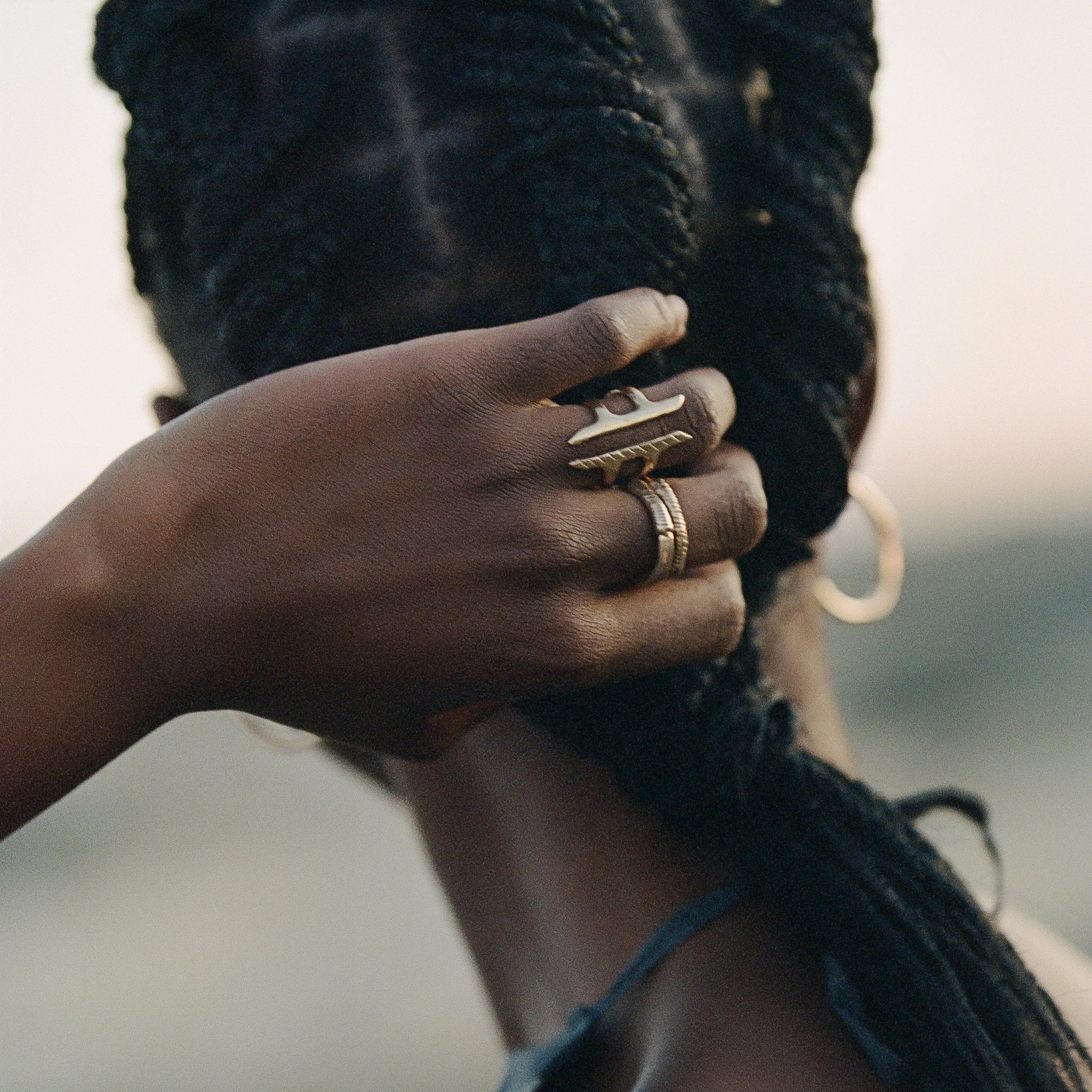 Model gathering her braids, wearing the Akash Shield Statement Ring with stacked rings.