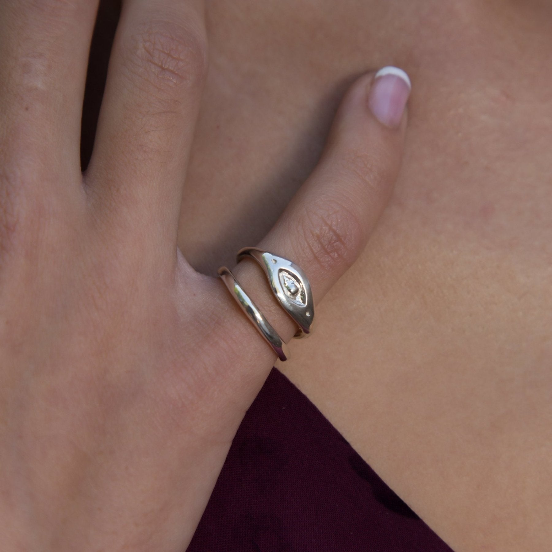 Hand resting on burgundy fabric wearing the Evil Eye Protection Ring stacked with a slim band.