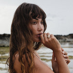 Model with long wavy hair by the sea, her hand at her lips wearing the Heritage Textured Signet Ring.