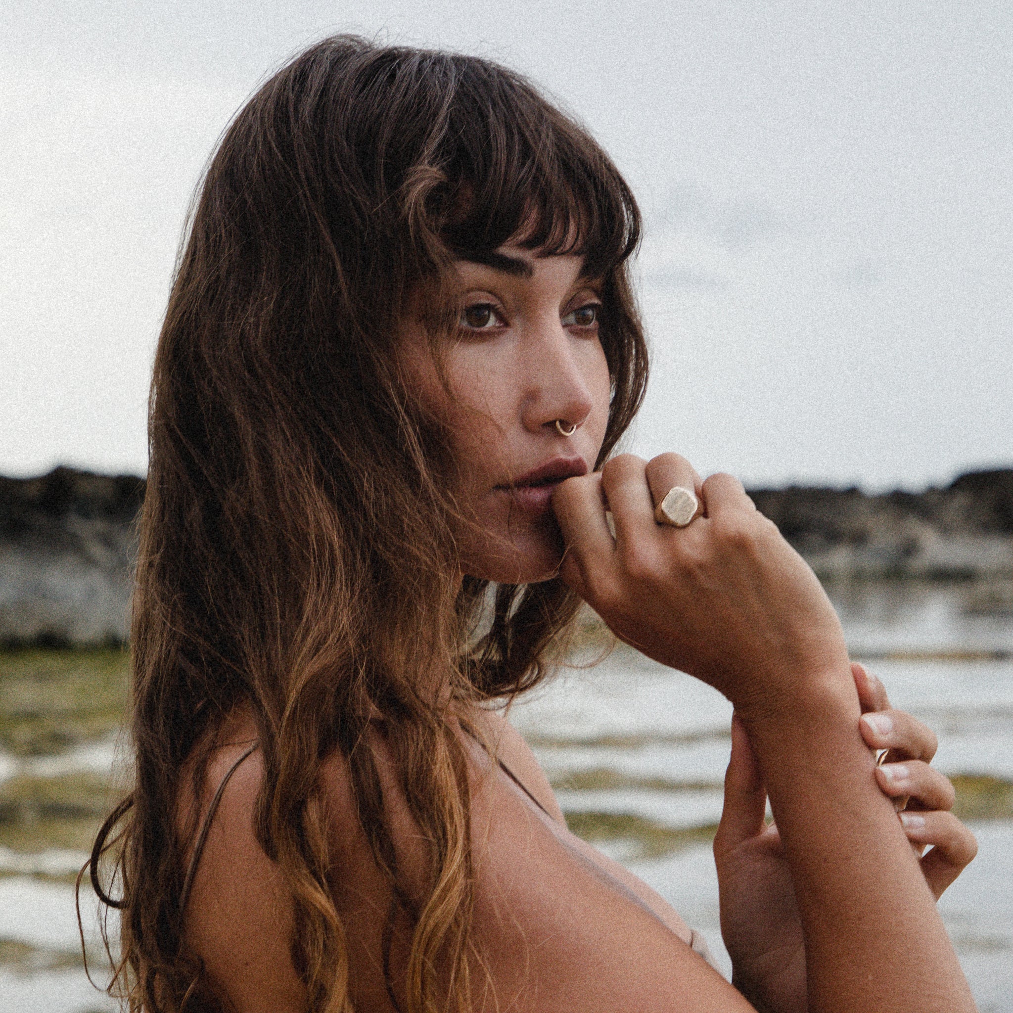 Model with long wavy hair by the sea, her hand at her lips wearing the Heritage Textured Signet Ring.
