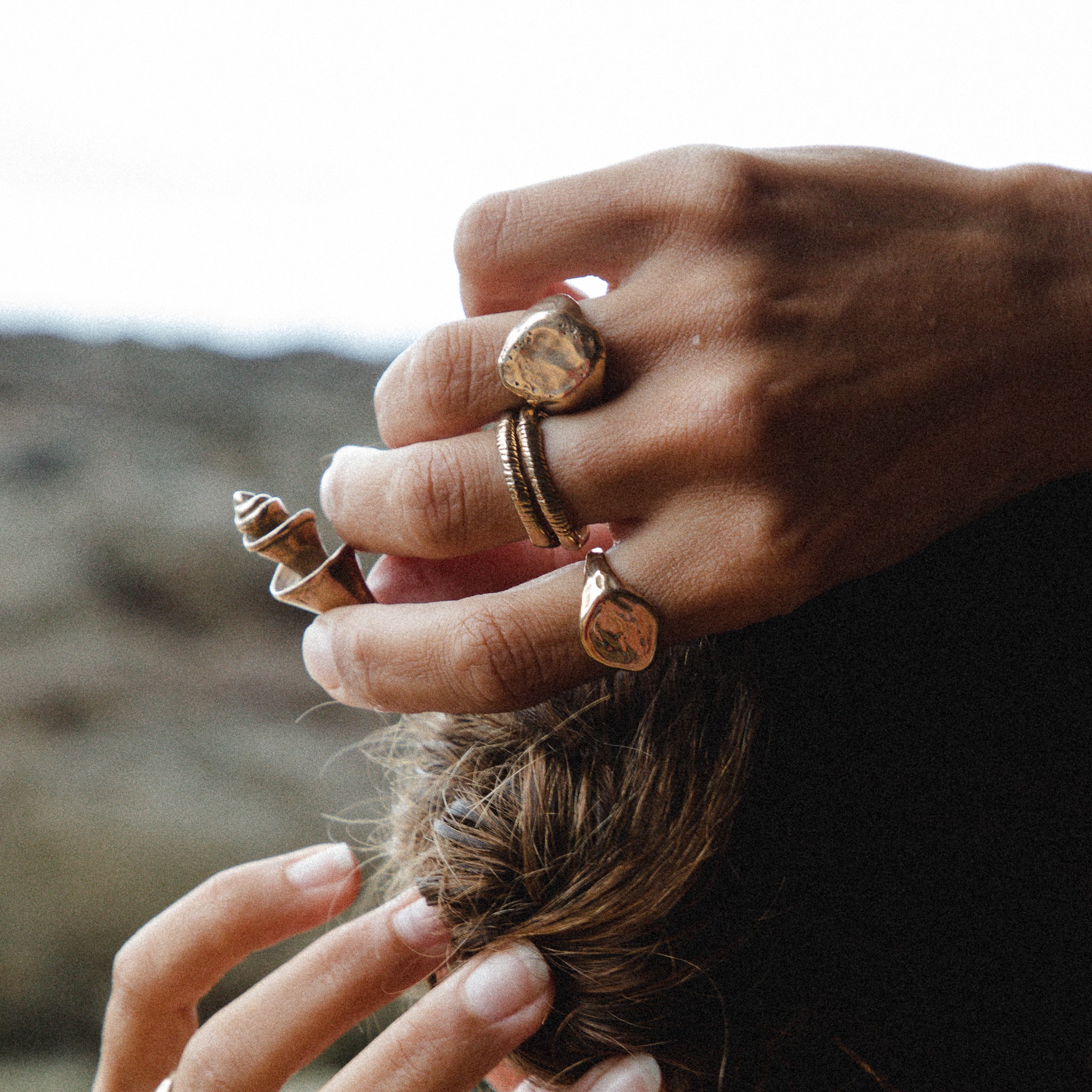 Hands gathering long hair, wearing the Heritage Textured Signet Ring stacked with other rings.