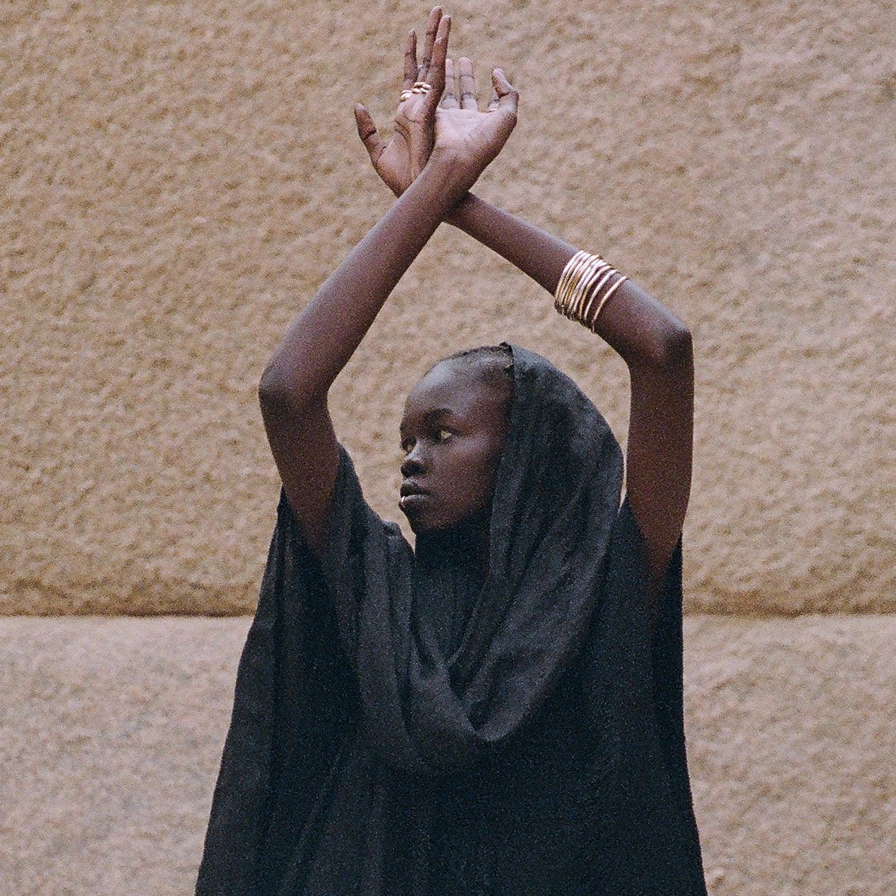 Rustic Bangles stacked on the wrist of a model with arms raised against a stone wall.