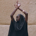 Rustic Bangles stacked on the wrist of a model with arms raised against a stone wall.