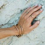 Rustic Bangles stacked on the wrist, hand resting on white rock.
