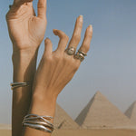 Hands raised against the sky in front of the pyramids of Giza, wearing the Scarab Ring and stacked Catori Life rings and cuffs