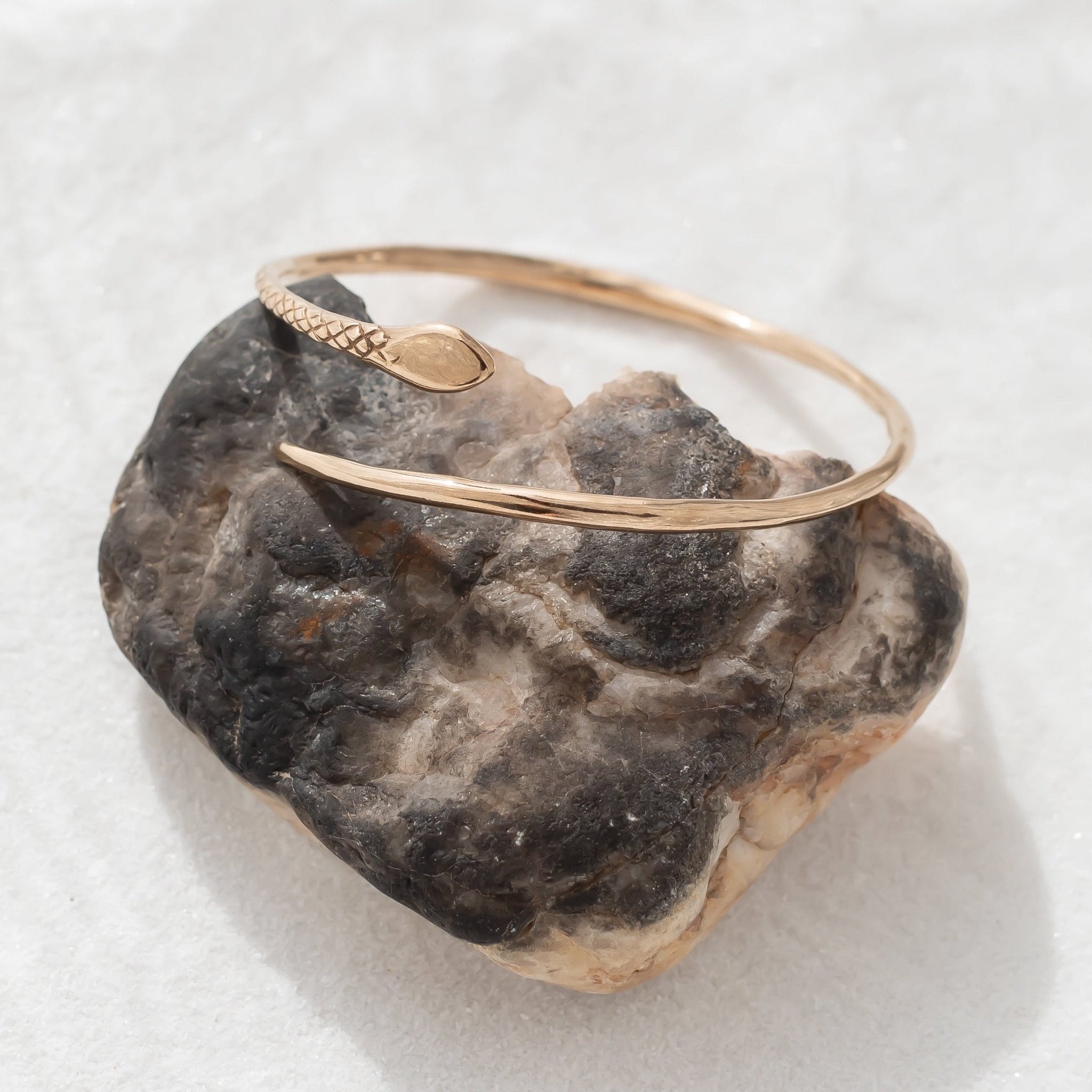 Serpent Snake Arm Cuff resting on a dark stone, showing the carved snake head.