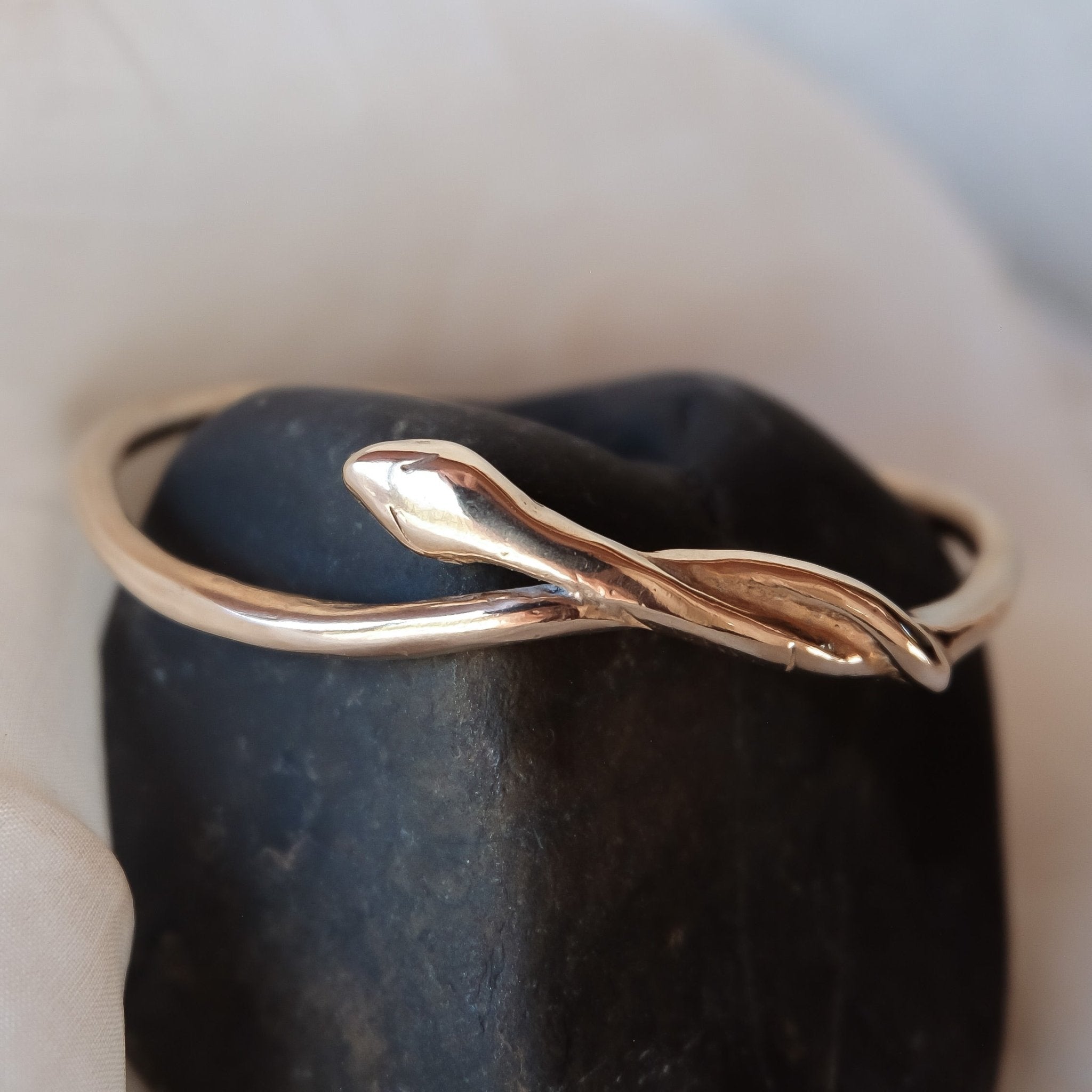 Serpent Snake Bangle in bronze displayed on a dark stone.