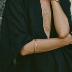 Serpent Snake Bangle worn on the arm of a model in a black wrap dress with layered necklaces.