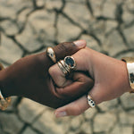Two hands clasped over cracked earth, wearing Catori Life rings including the Smoky Quartz Signet Ring
