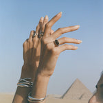 Hands raised in front of the pyramids of Giza, wearing the Smoky Quartz Signet Ring and stacked Catori Life rings