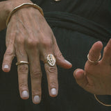 Model's hands against dark fabric wearing the Venus Signet Ring, a carved goddess signet, with organic bangles and rings.