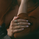 Hands resting on a rust-colored sweater, wearing the Wild Rose Ring stacked with Catori Life rings