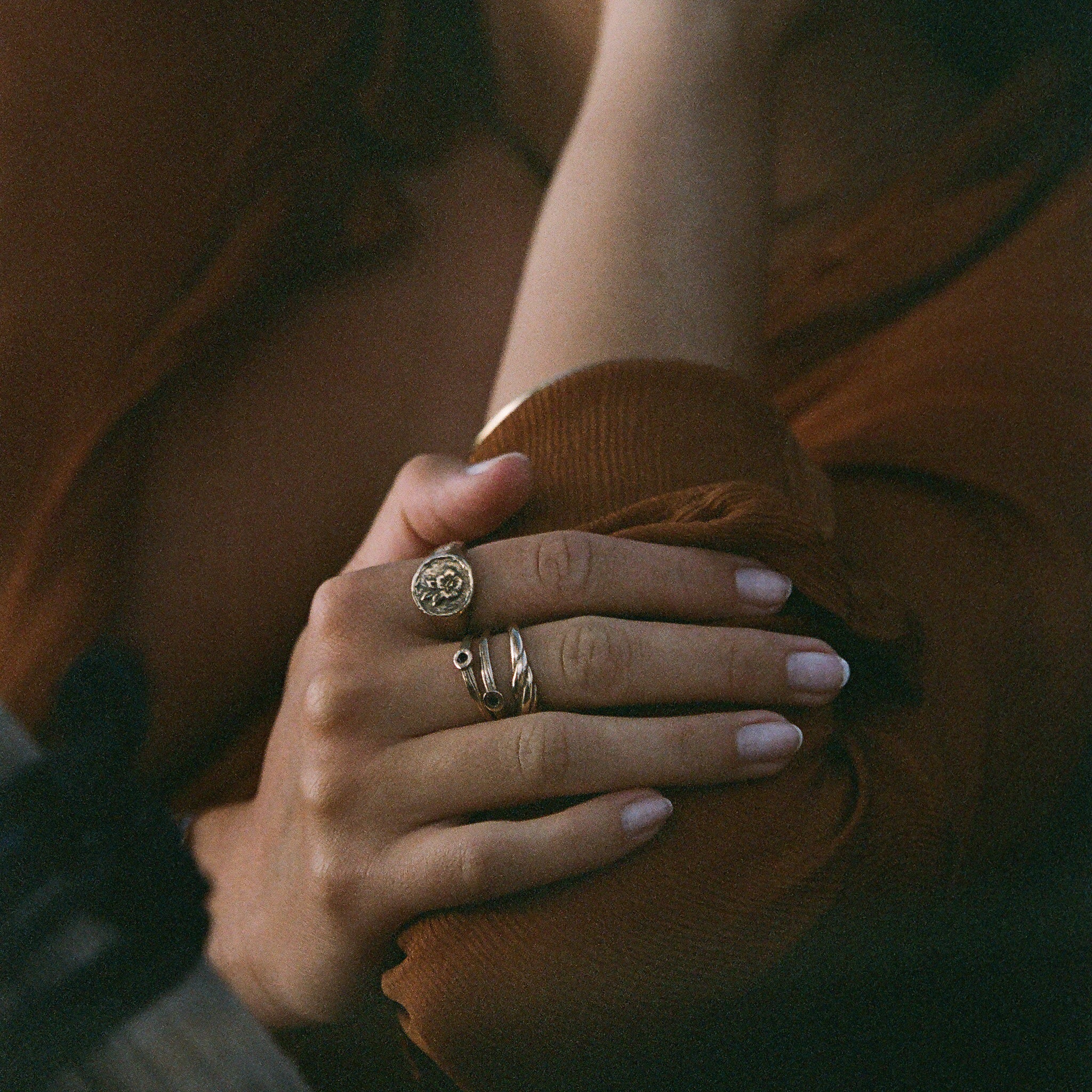 Hands resting on a rust-colored sweater, wearing the Wild Rose Ring stacked with Catori Life rings